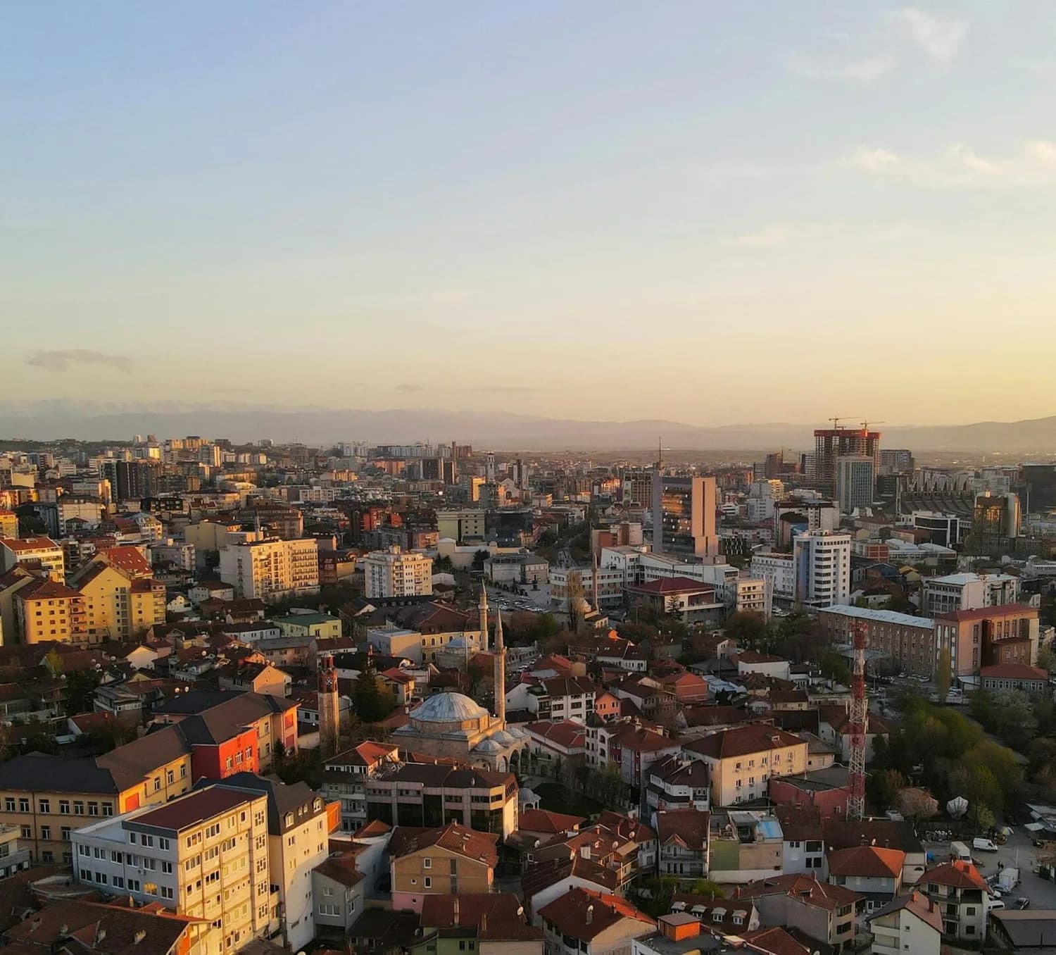 Luftaufnahme von Pristina Kosovo bei Sonnenuntergang mit Moschee, Minarett, Wohnhäusern und moderner Stadtsilhouette