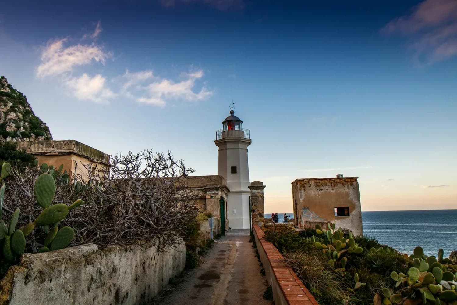 Leuchtturm an der Küste von Palermo mit verwitterten Gebäuden, Kakteen und Meer im Abendlicht