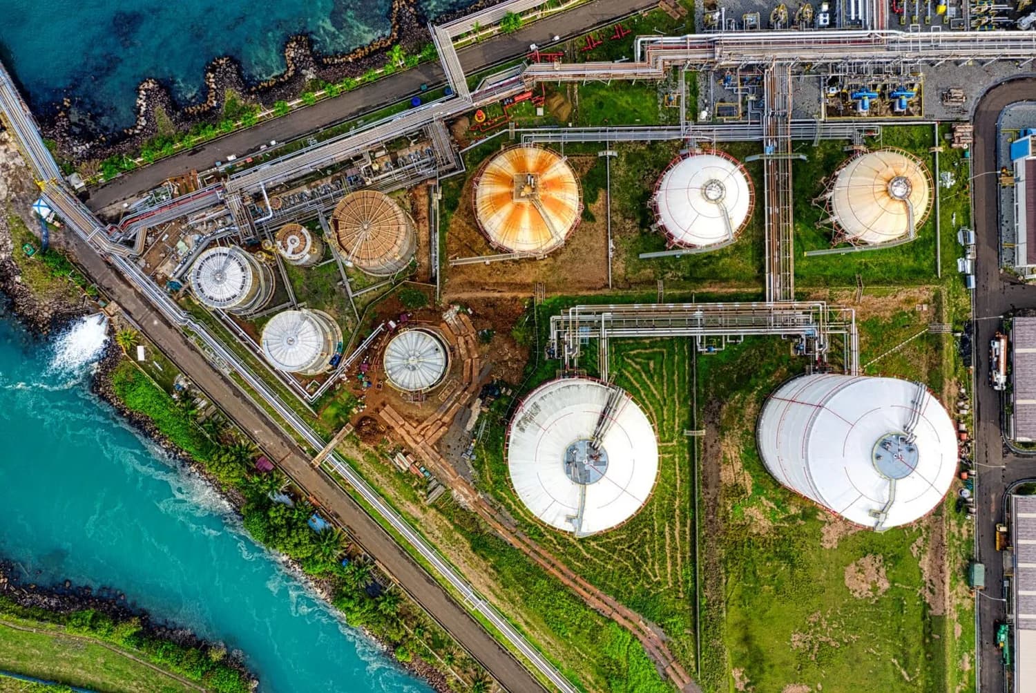 Luftaufnahme einer Küsten-Tanklageranlage mit großen zylindrischen Lagertanks, Rohrleitungen und Infrastruktur für nachhaltige Kraftstofflagerung