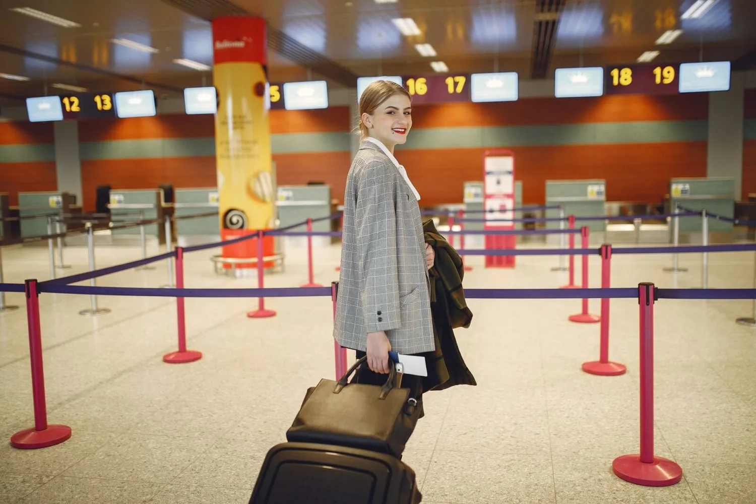 Frau mit Trolley und Handtasche im Flughafen-Check-in Bereich, Gepäck und Koffer in der Schlange vor Check-in-Schaltern