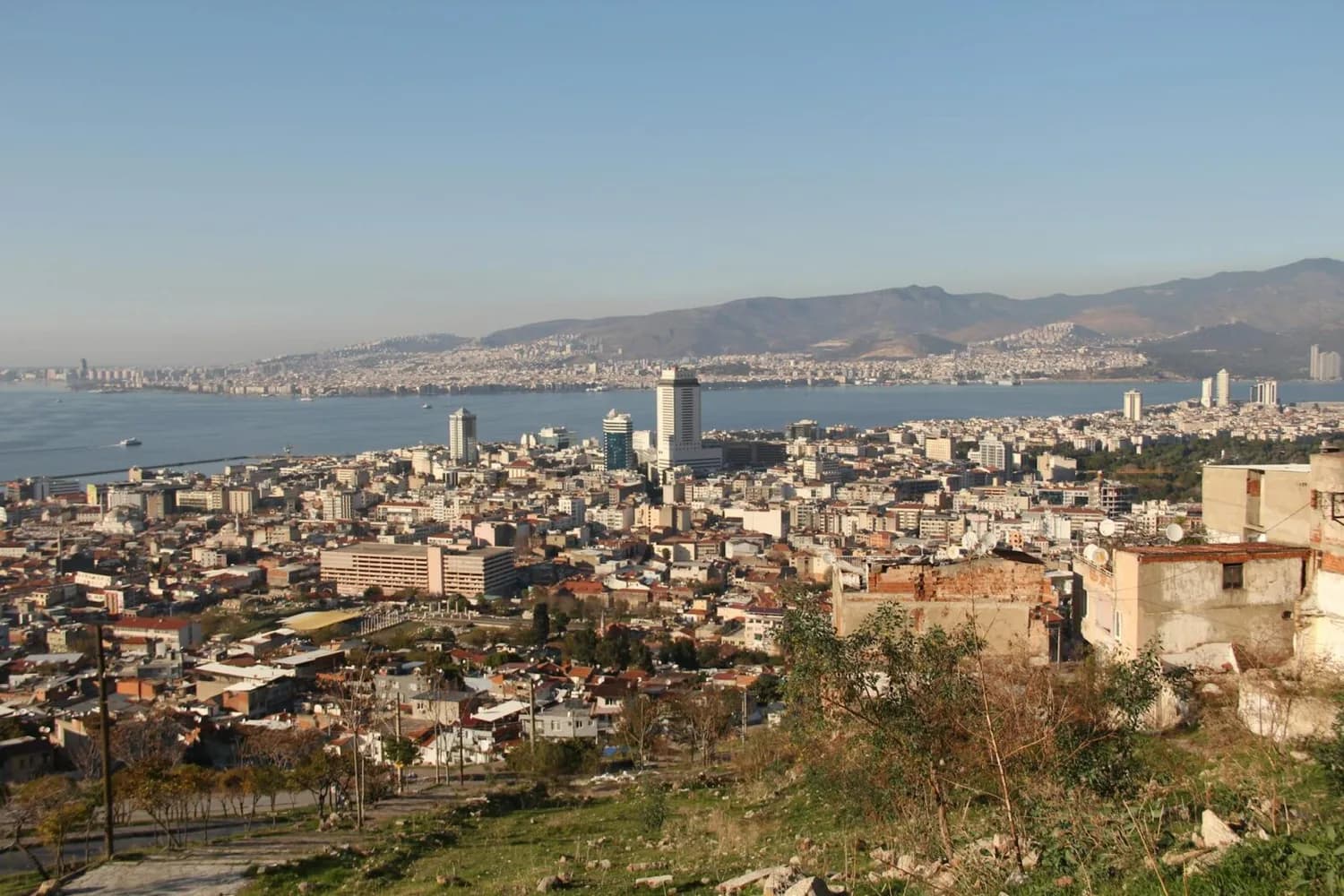 Panorama von İzmir mit Stadtzentrum, Küste und Hafen, Hochhäusern und dicht bebauten Wohnvierteln vor bergiger Kulisse