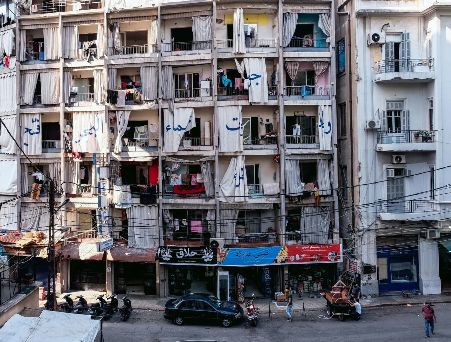 Fassadenansicht eines mehrstöckigen Wohngebäudes in Beirut mit offenen Balkonen, hängenden Vorhängen, Wäscheleinen und Geschäften im Erdgeschoss