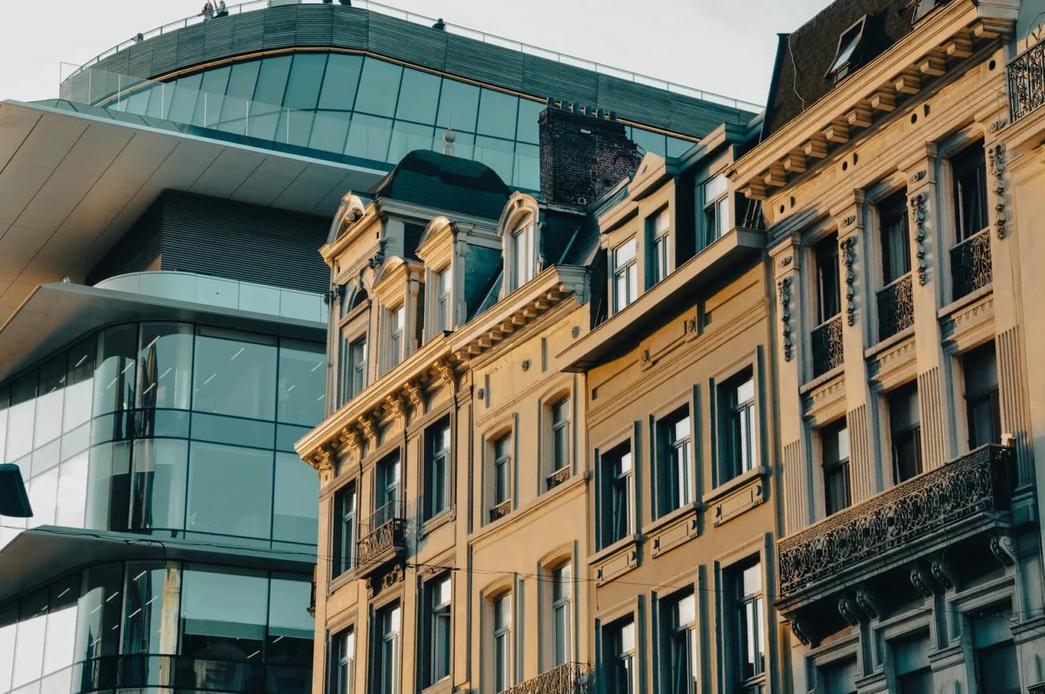 Historische Fassaden und Balkone im Vordergrund vor moderner Glasfassade in Brüssel, Belgien