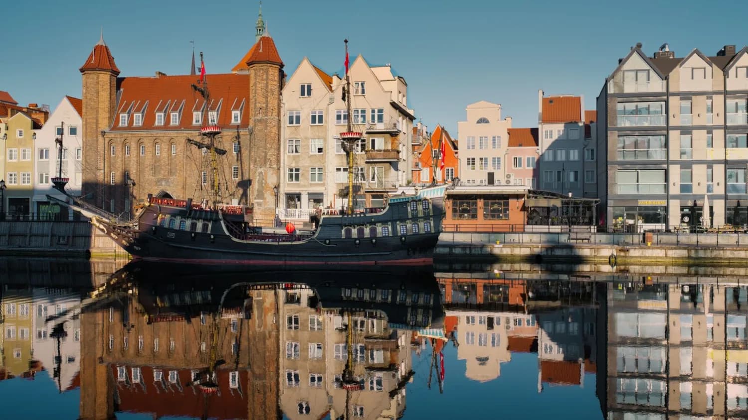 Historisches Segelschiff am Kai der Danziger Motława mit bunten Giebelhäusern und Spiegelung im Wasser