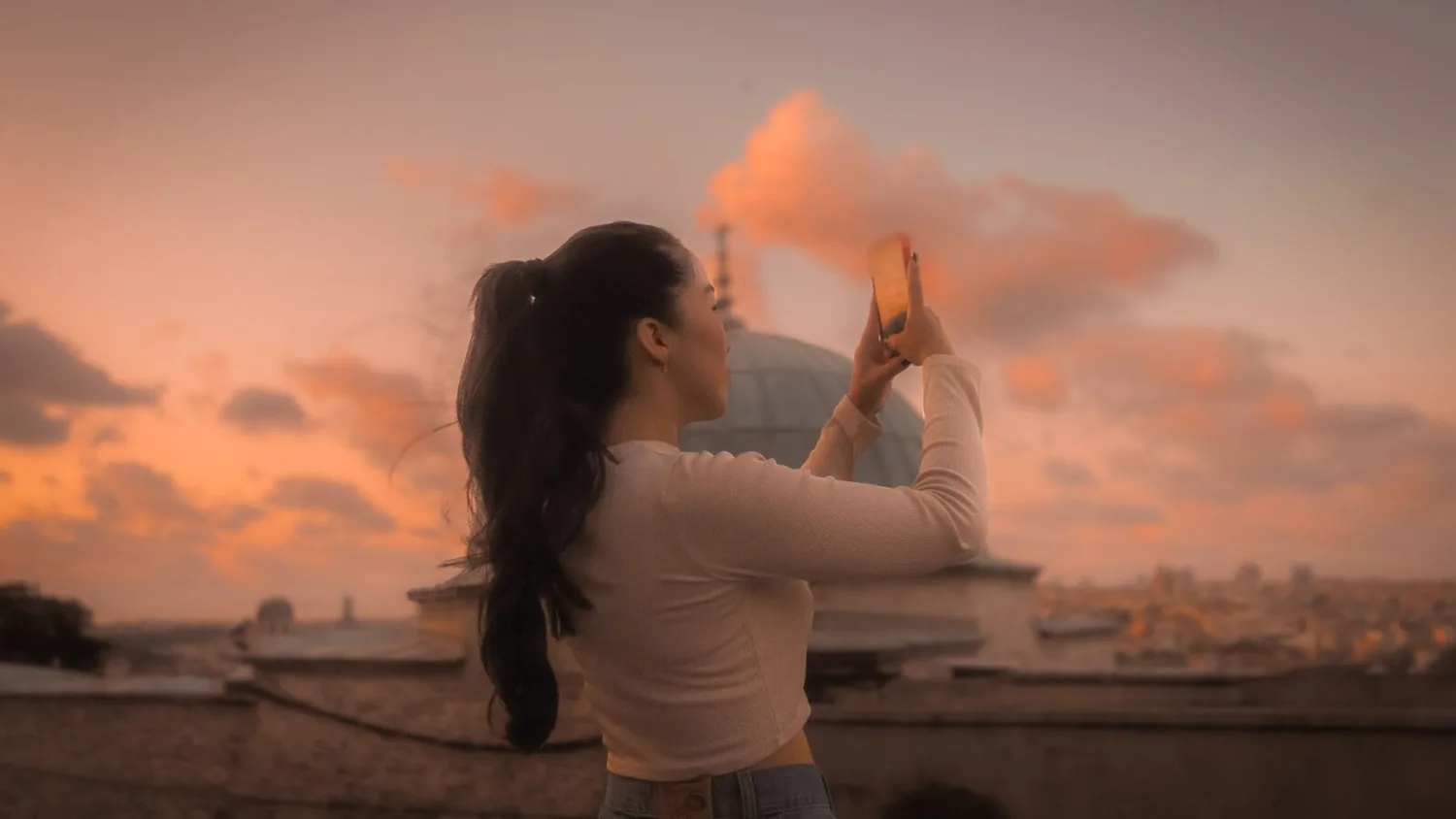 Frau auf Reisen fotografiert Sonnenuntergang mit Smartphone vor Stadtkulisse und Kuppel