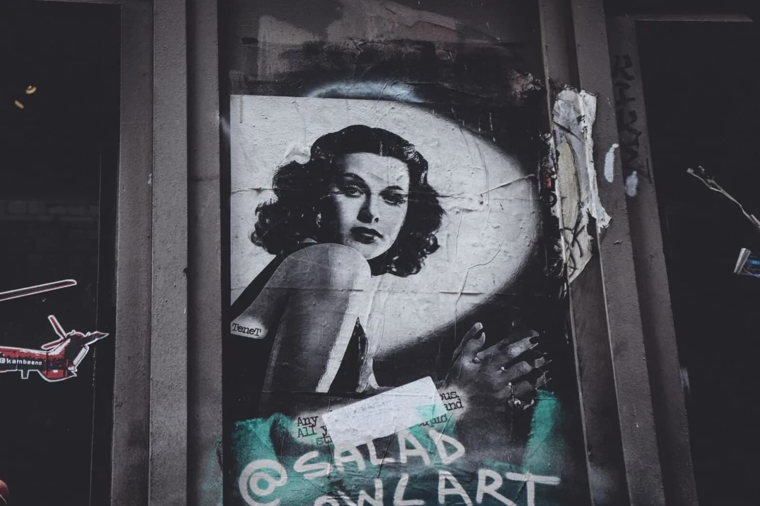 Schwarzweiß-Poster einer glamourösen Frau im Stil der goldenen Zwanziger, auf einer verwitterten Straßenwand mit Graffiti und übereinander geklebten Papierstücken.