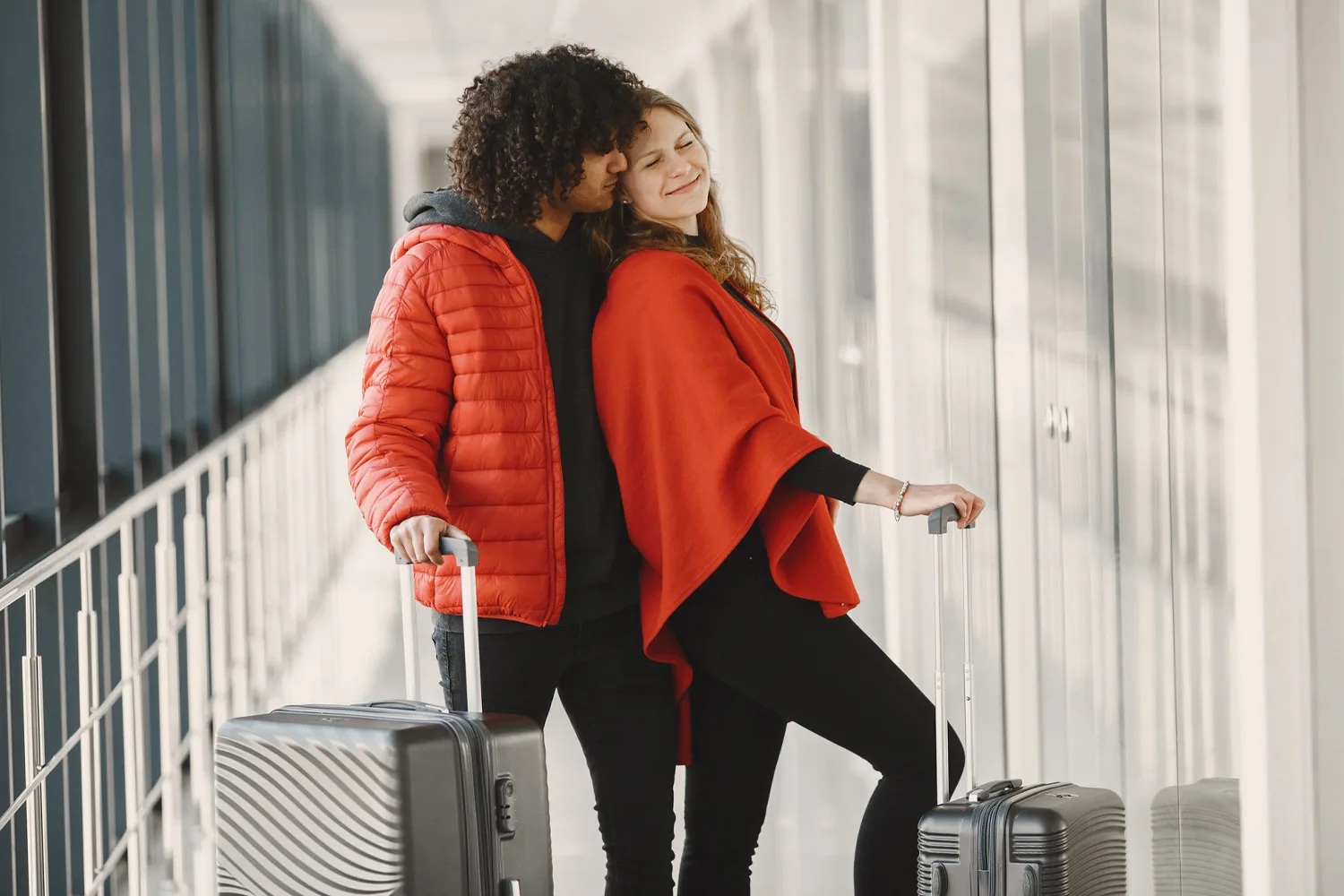 Paar mit Rollkoffern umarmt sich auf einer Gangway in einem Flughafen- oder Hafenterminal