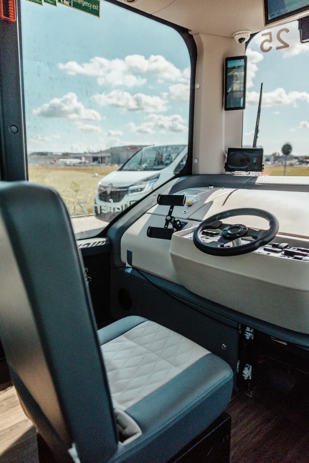 Innenraum eines autonomen Shuttle ZRH mit Fahrersitz, Lenkrad und Monitoren, Blick durch die Frontscheibe auf Flughafen und wartendes Fahrzeug