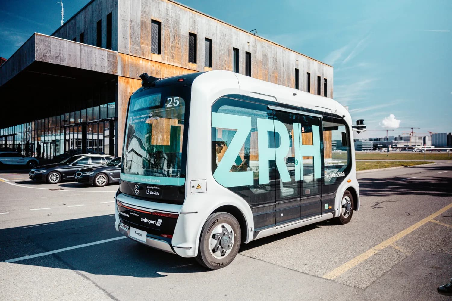 Autonomer Shuttle-Bus mit grossem ZRH-Schriftzug am Flughafen Zürich, weisser Elektro-Shuttle neben Terminalgebäude