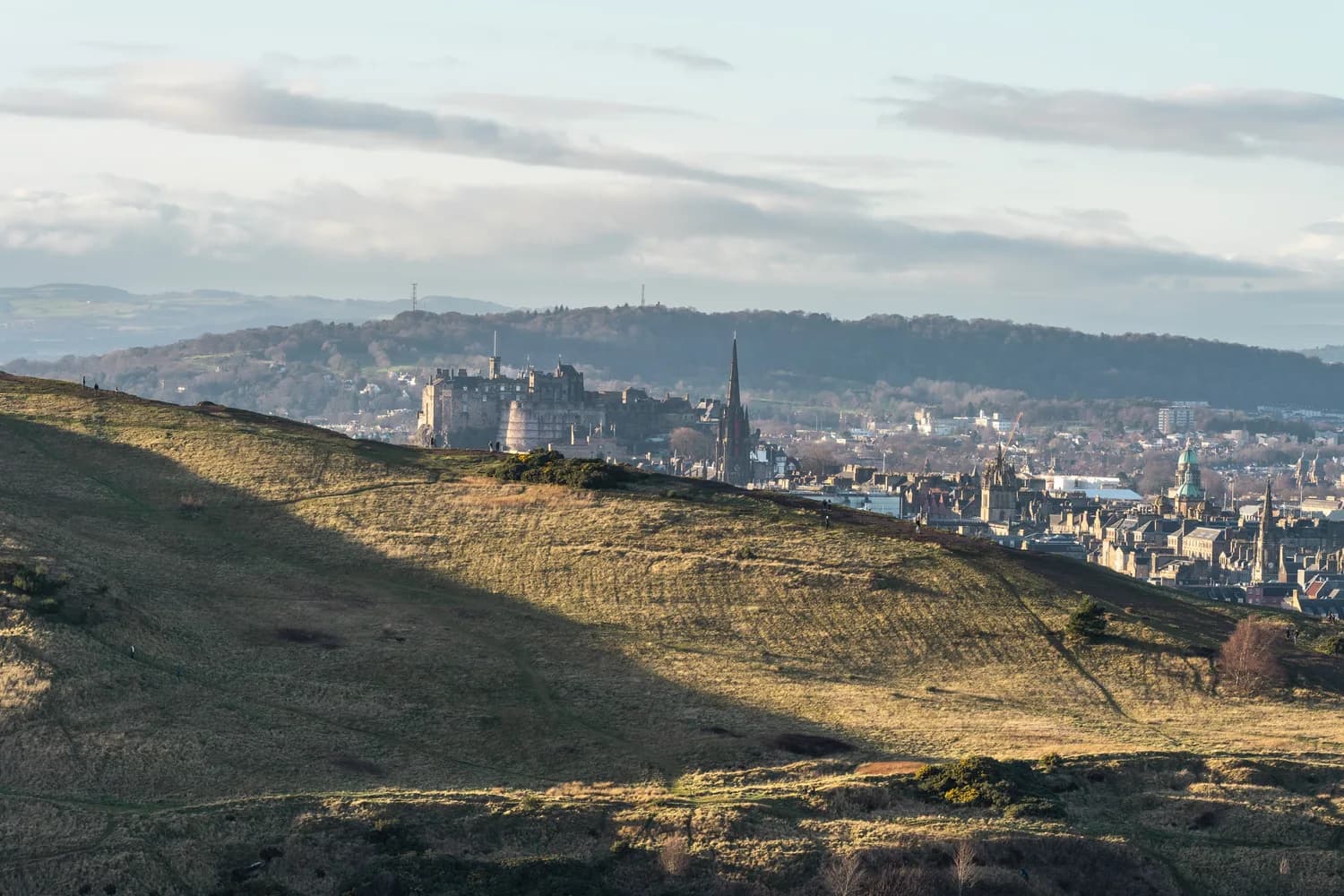 Blick auf Edinburghs historische Skyline mit Edinburgh Castle, Kirchturmspitzen und hügeliger Vorlandschaft bei weichem Tageslicht