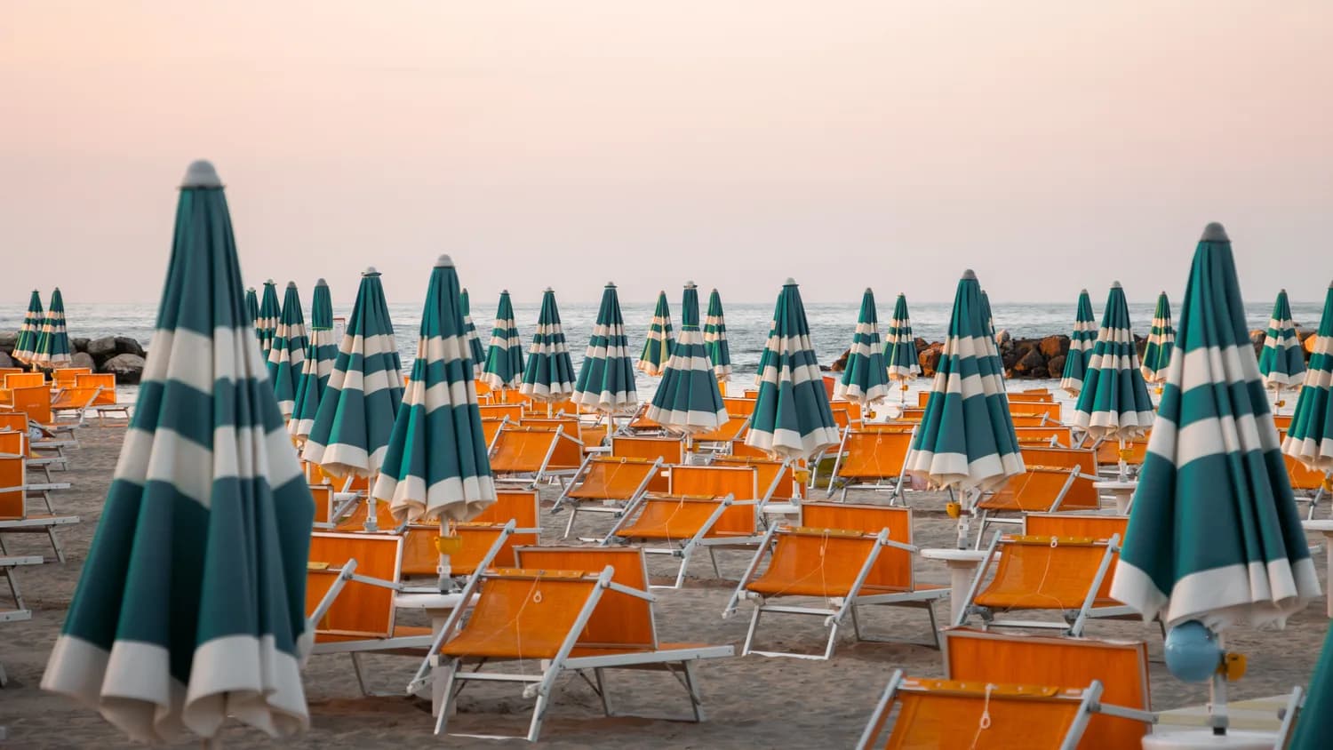 Strand von Rimini mit Reihen grüner weißer Sonnenschirme und orangen Liegestühlen bei Sonnenuntergang