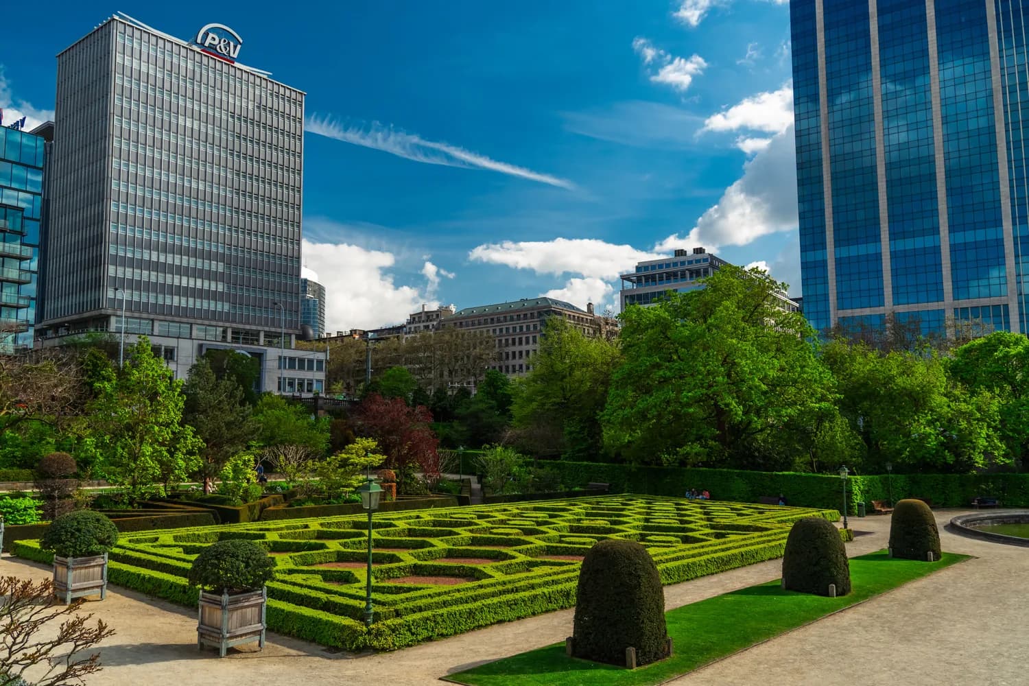 Parkanlage mit formalem Heckengarten und skulpturierten Büschen vor modernen Wolkenkratzern in Brüssel