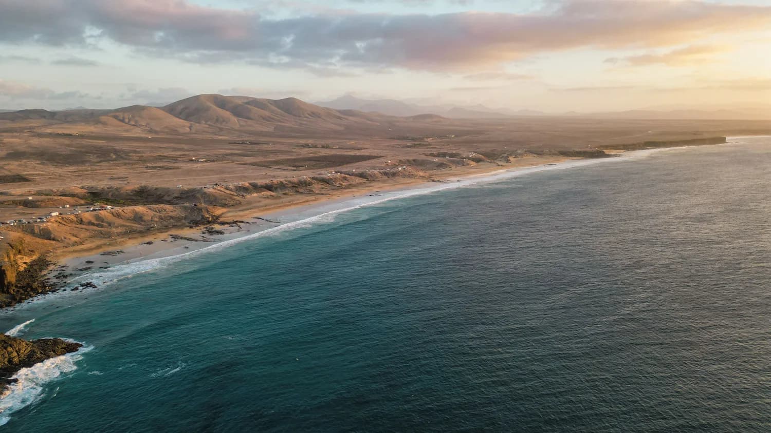 Weitläufiger Sandstrand von Fuerteventura an der Küste der Kanaren mit ruhigem Meer und kahler Dünenlandschaft bei Sonnenuntergang