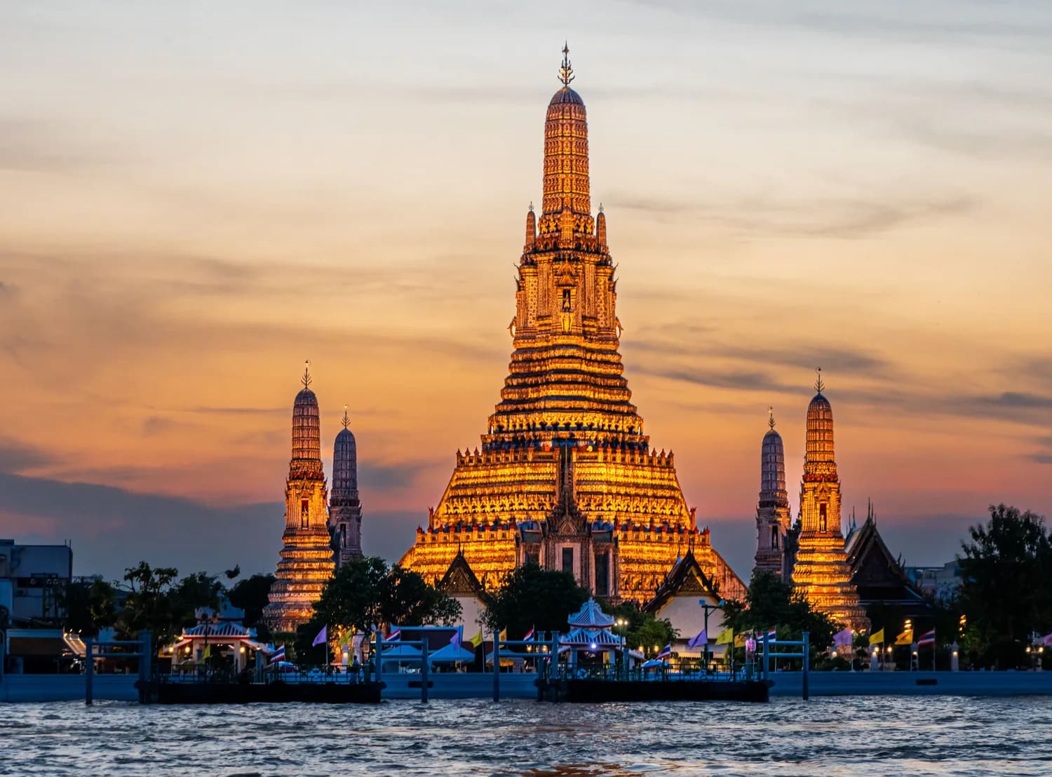 Wat Arun Tempel am Chao Phraya Flussufer bei Sonnenuntergang, beleuchteter Turm und Pagoden in Bangkok
