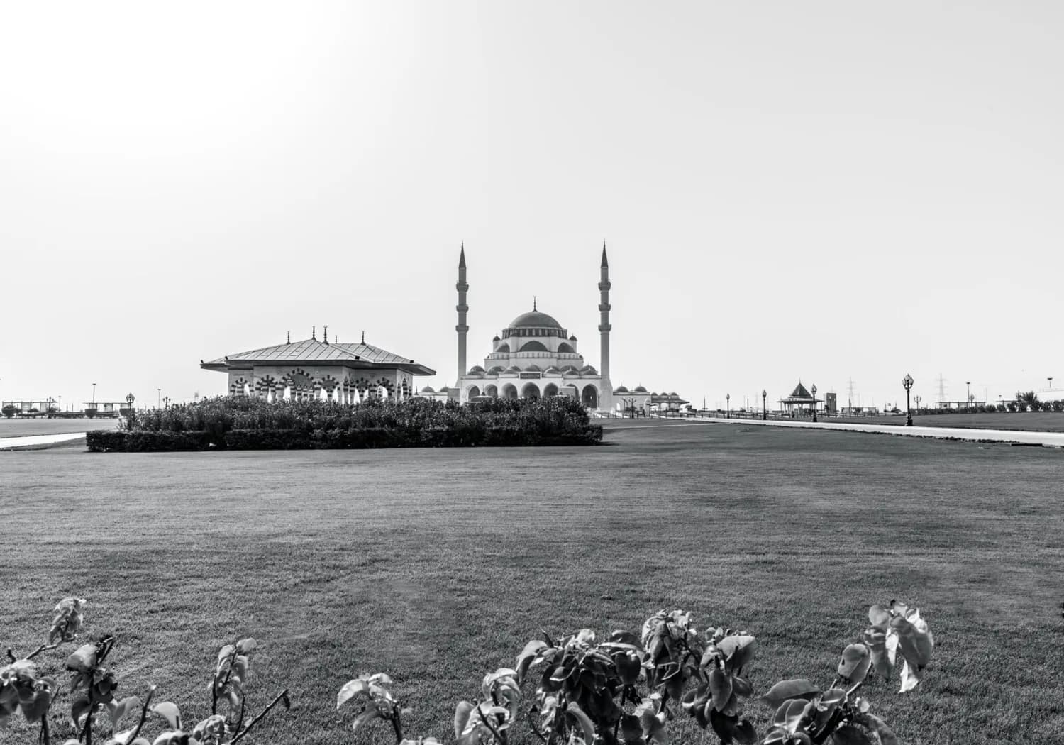 Großes Parkgelände mit Blick auf die Al Noor Mosque in Sharjah, zwei schlanke Minarette und Pavillon im Vordergrund, gepflegte Rasenflächen und Spazierwege