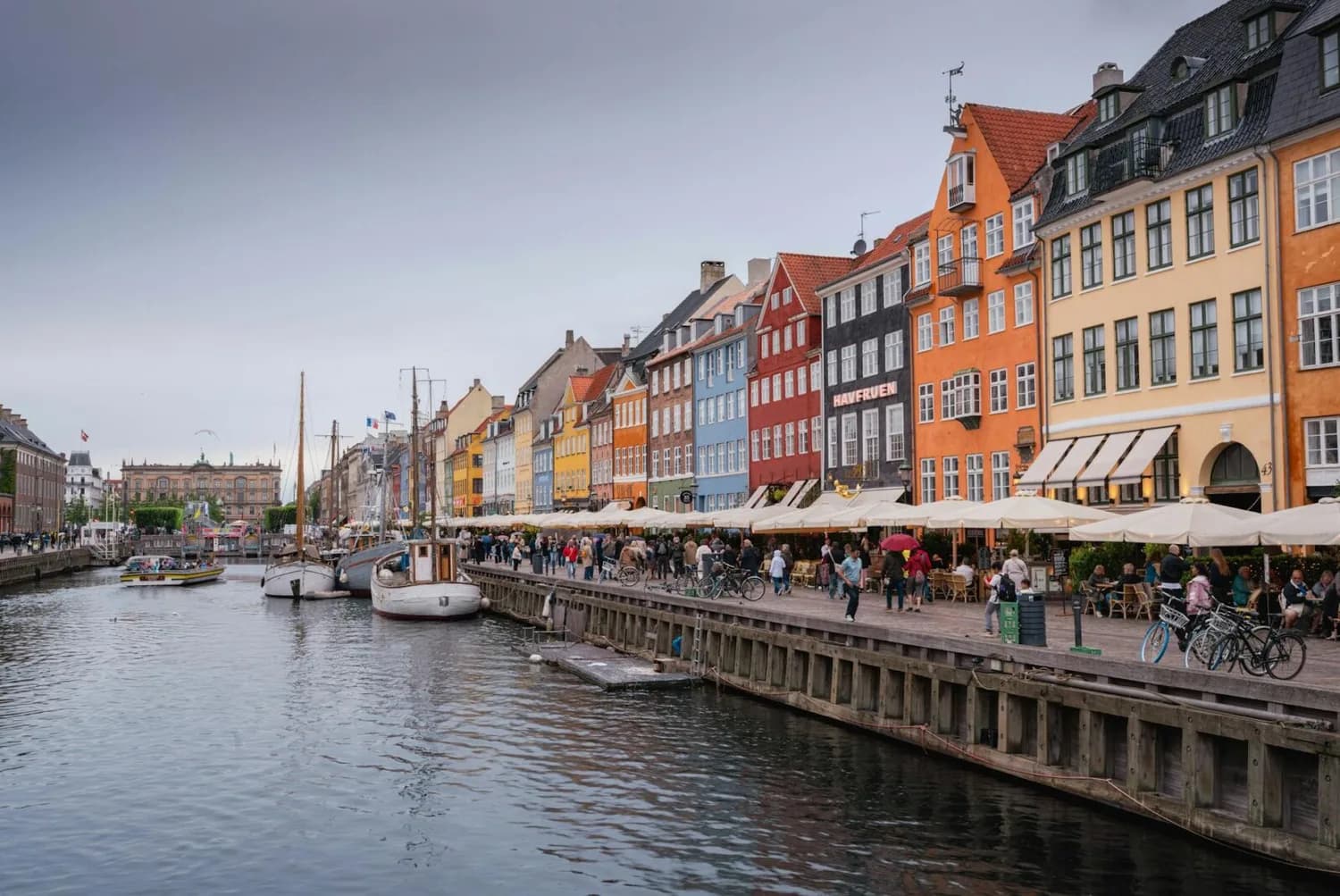 Bunte Giebelhäuser am Nyhavn-Kanal in Kopenhagen mit Booten, Uferpromenade, Menschen und Straßencafés