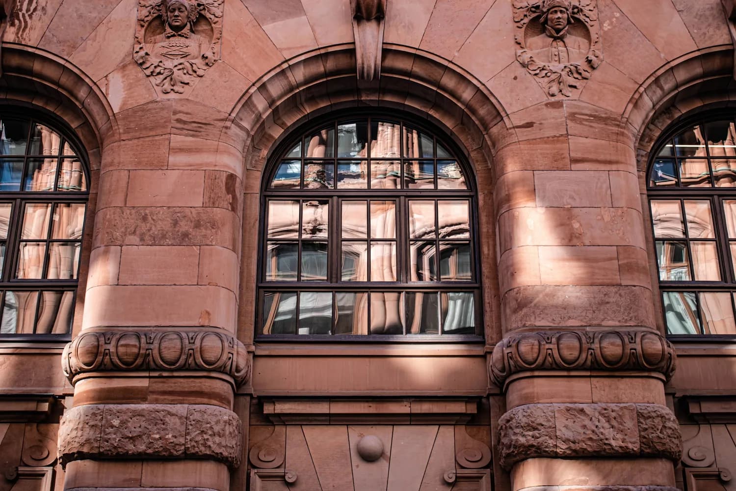Historische Sandsteinfassade in Stockholm mit Rundbogenfenstern, dekorativen Säulen und Ornamenten, Reflexionen in Fensterscheiben