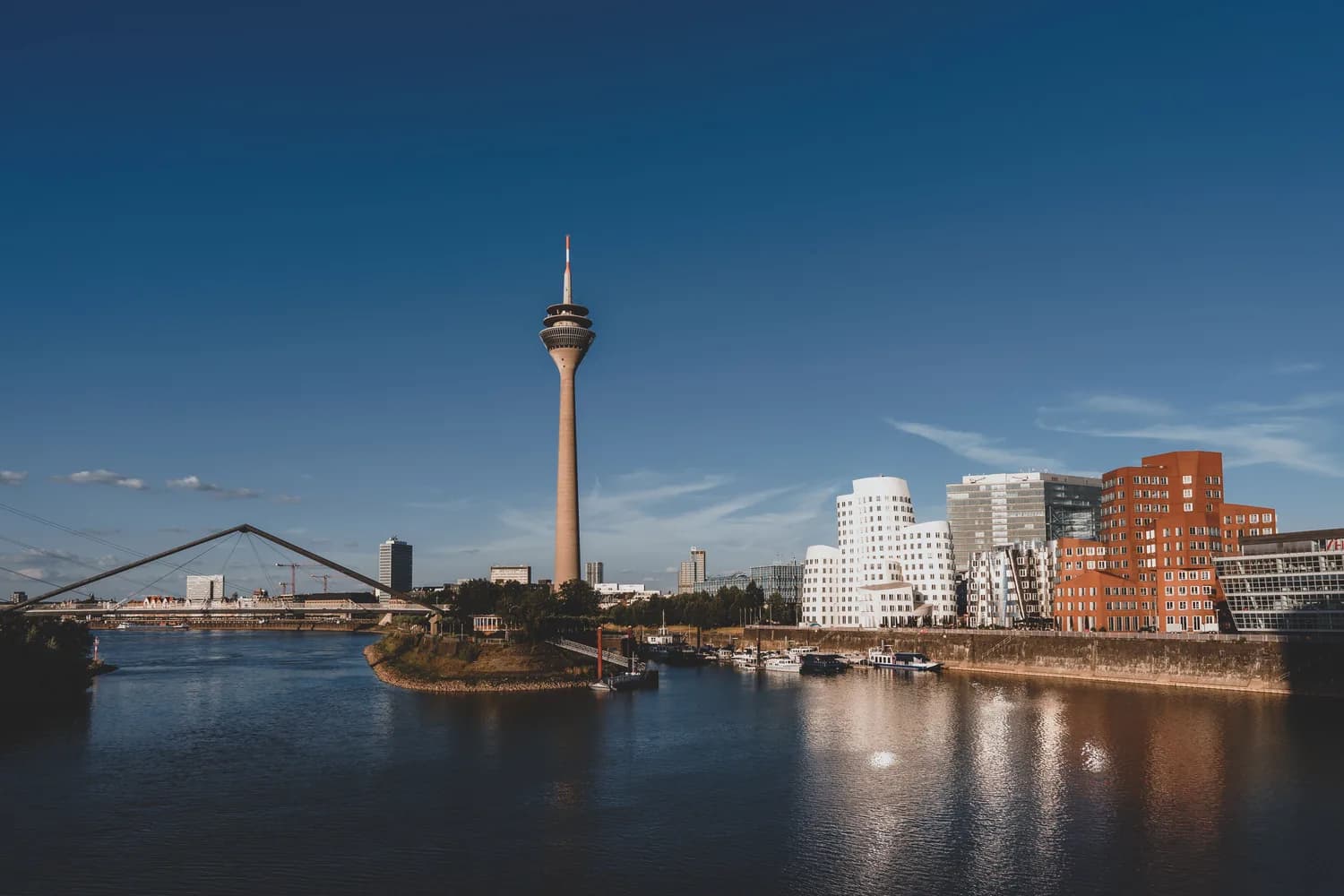 Düsseldorfer Rheinturm und moderne Architektur der MedienHafen-Uferpromenade mit Rheinkniebrücke und Spiegelungen im Rhein