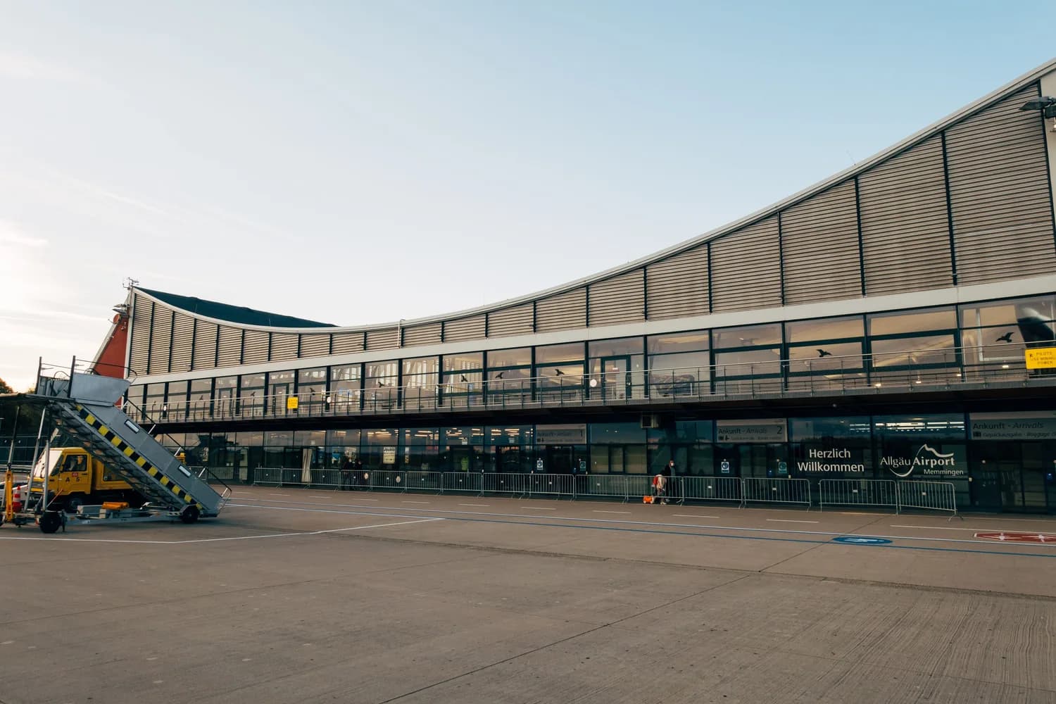 Außenansicht Terminal Allgäu Airport Memmingen mit Flugsteigtreppe, Glasfassade und Beschilderung Herzlich Willkommen