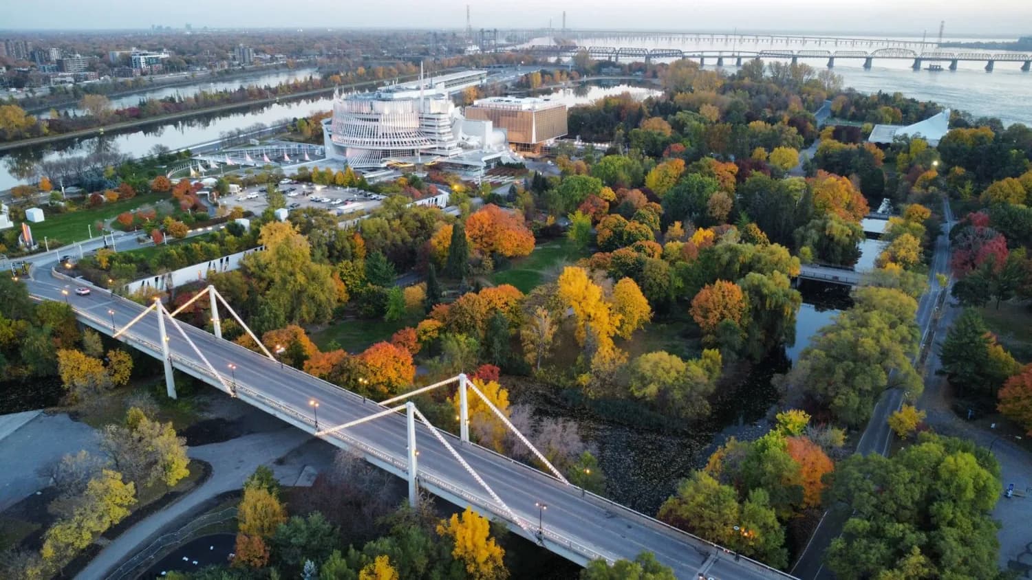 Luftaufnahme der Île Sainte-Hélène in Montreal mit beleuchteter Hängebrücke, herbstlich buntem Parkwald und Kulturzentrum am Sankt-Lorenz-Strom