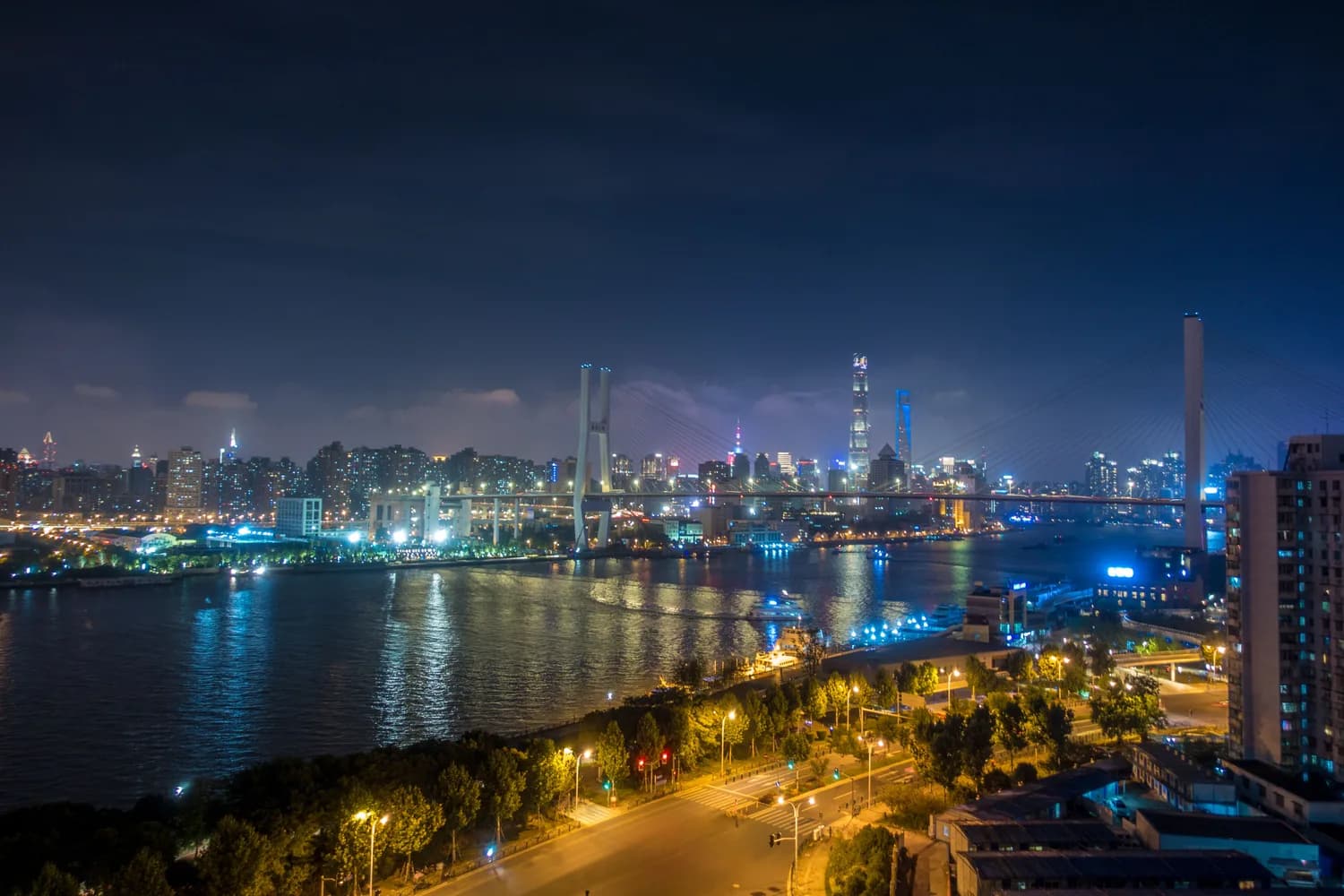 Shanghai Pudong Skyline bei Nacht mit beleuchteter Brücke und Spiegelung im Fluss, städtische Hochhäuser und Lichterpromenade