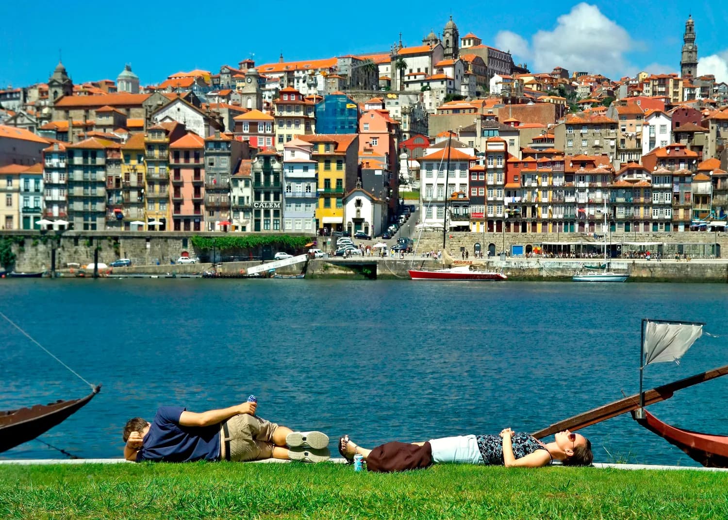 Pärchen entspannt auf Gras am Douro-Ufer in Porto mit bunten Häusern der Ribeira und Booten im Fluss
