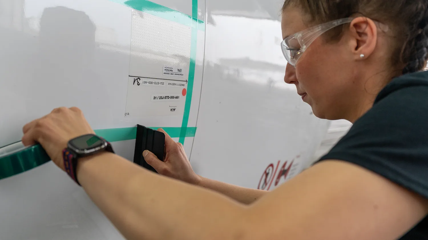 Frau mit Schutzbrille bringt grünes Klebeband auf Flugzeugrumpf auf und glättet Patch beim Aeroshark-Test
