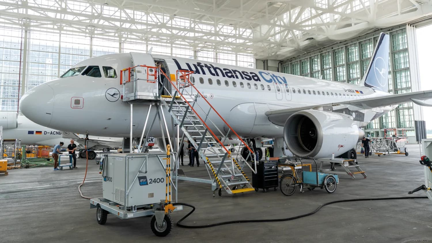 Lufthansa City Flugzeug im Hangar mit Wartungsleiter und mobilen Treppen, Techniker prüfen Triebwerk und Bordausrüstung