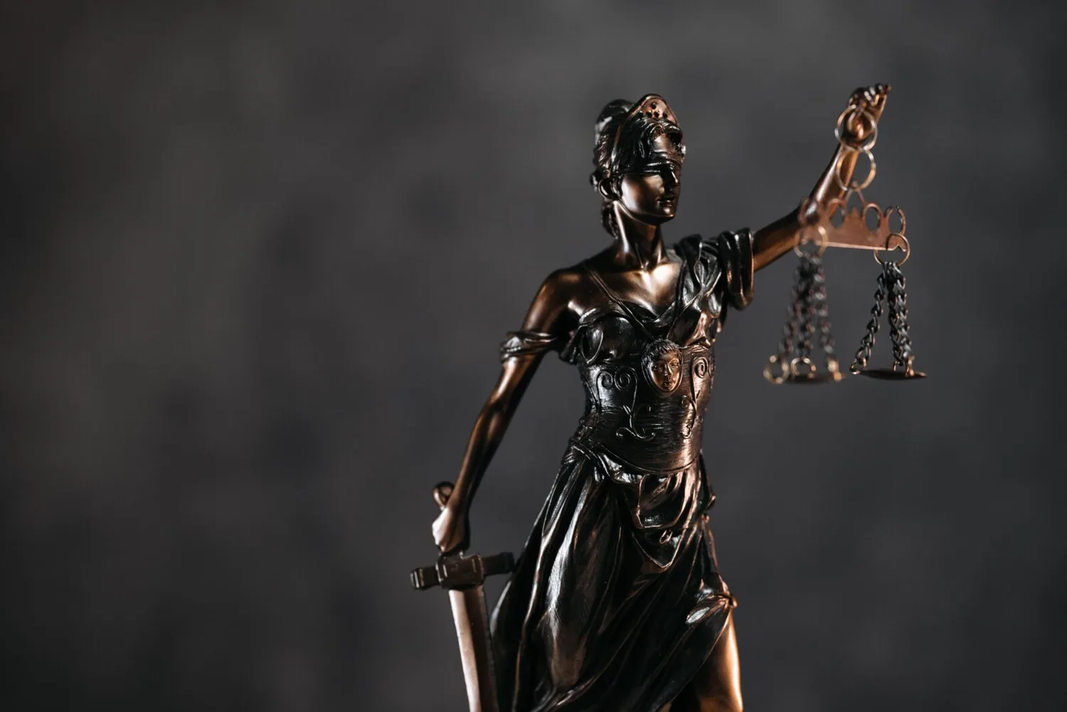 Justitia-Statue mit Waage und Schwert vor dunklem Hintergrund, Symbol für Gericht, Klage und Rechtsprechung
