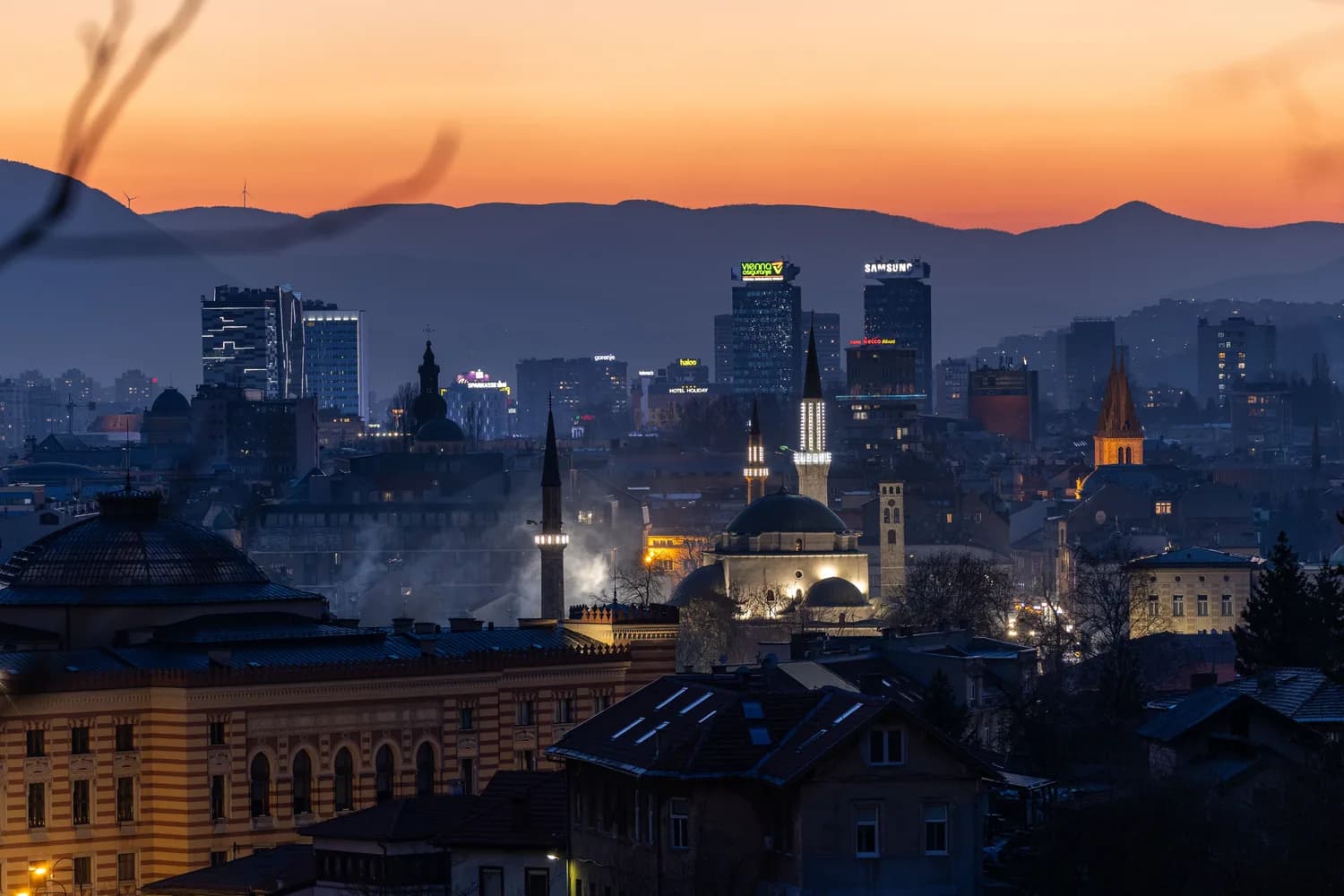 Stadtpanorama von Sarajevo in der Abendstimmung mit Minaretten und Bergen im Hintergrund