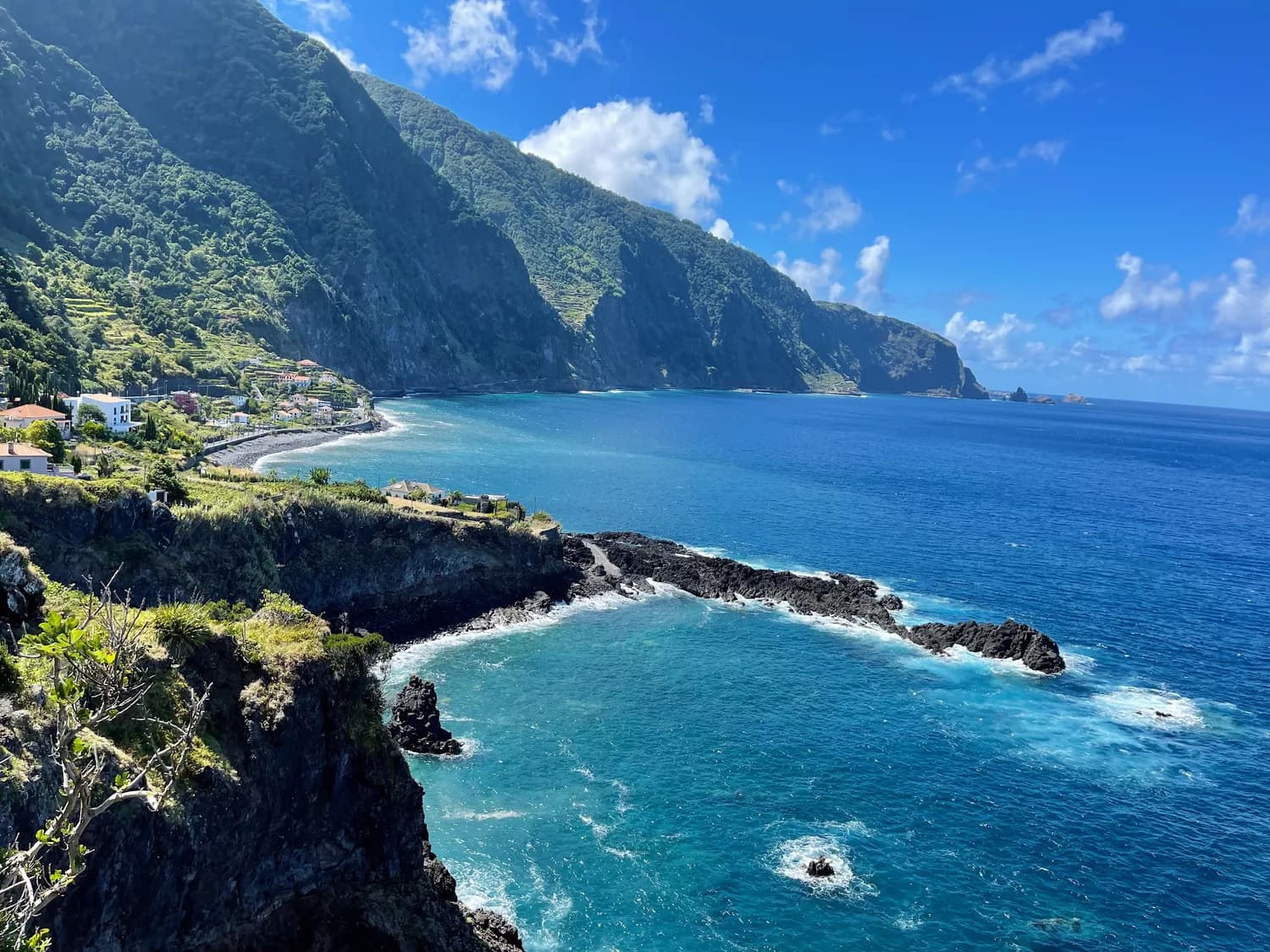 Steile Küste und Klippen bei Seixal auf Madeira mit türkisblauem Meer, Felsenriff und kleinen Häusern am Ufer