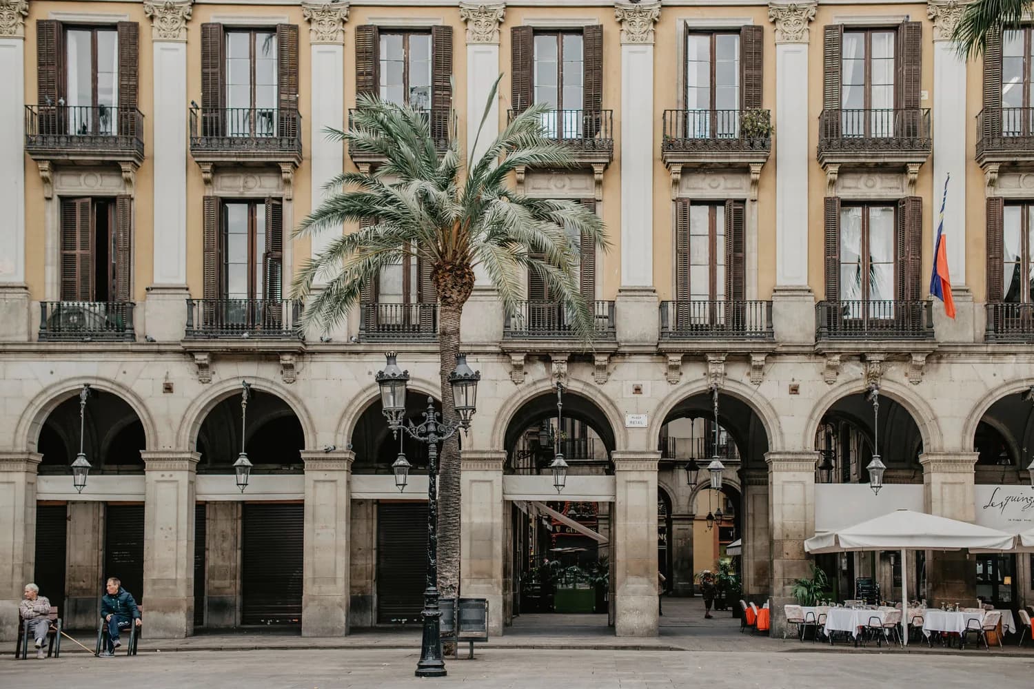 Placa Reial Barcelona mit Arkadenfassade, Balkonen, Palmen und Straßencafé in historischer Stadtarchitektur