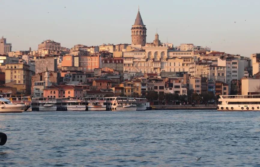 Blick auf den Bosporus mit Anlegern und Fähren, Galataturm und dicht bebauter Altstadt von Istanbul bei Sonnenlicht