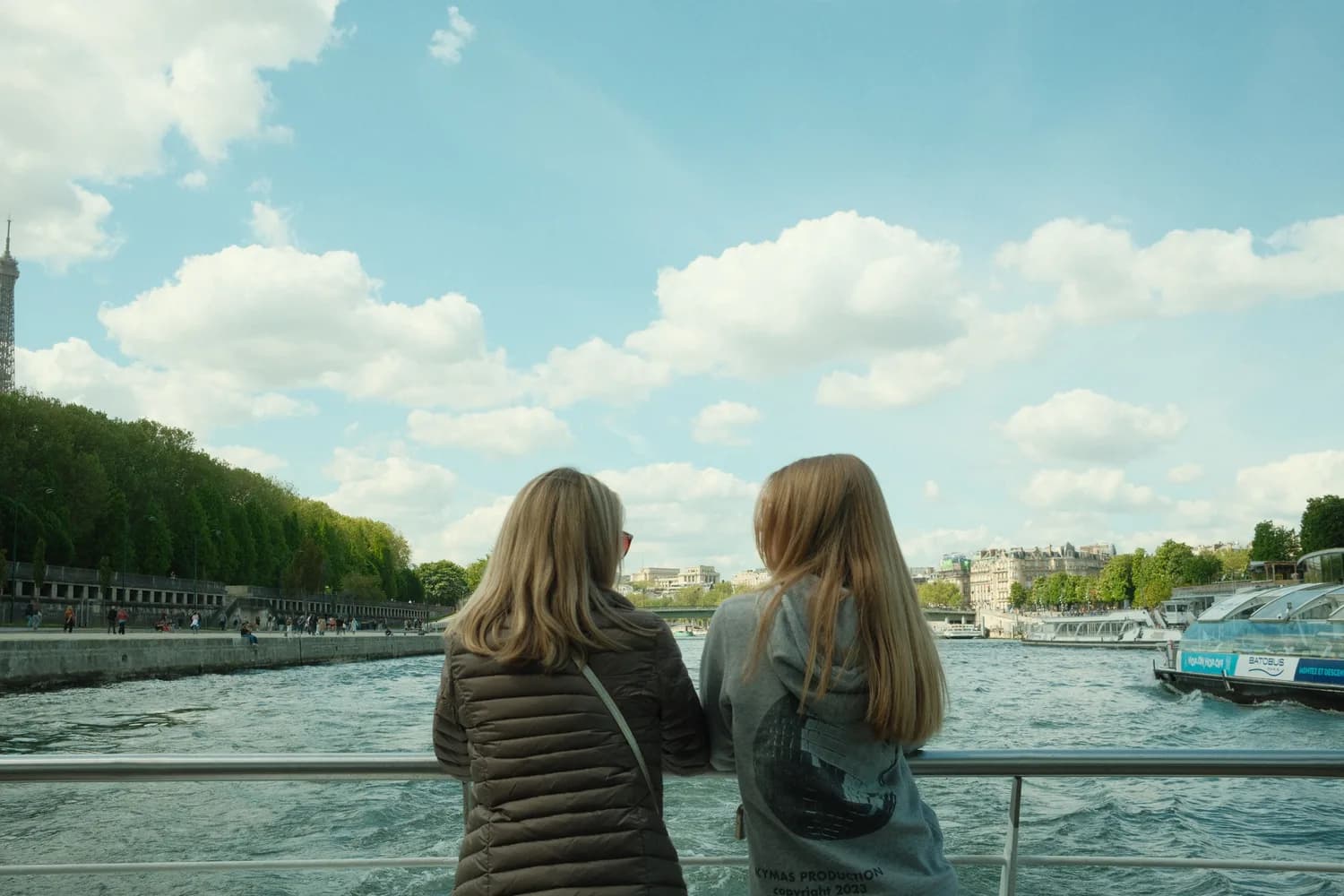 Zwei Frauen von hinten auf einer Bootstour auf der Seine mit Blick auf Uferpromenade, Passagierboote und grünen Parkanlagen in Brüssel