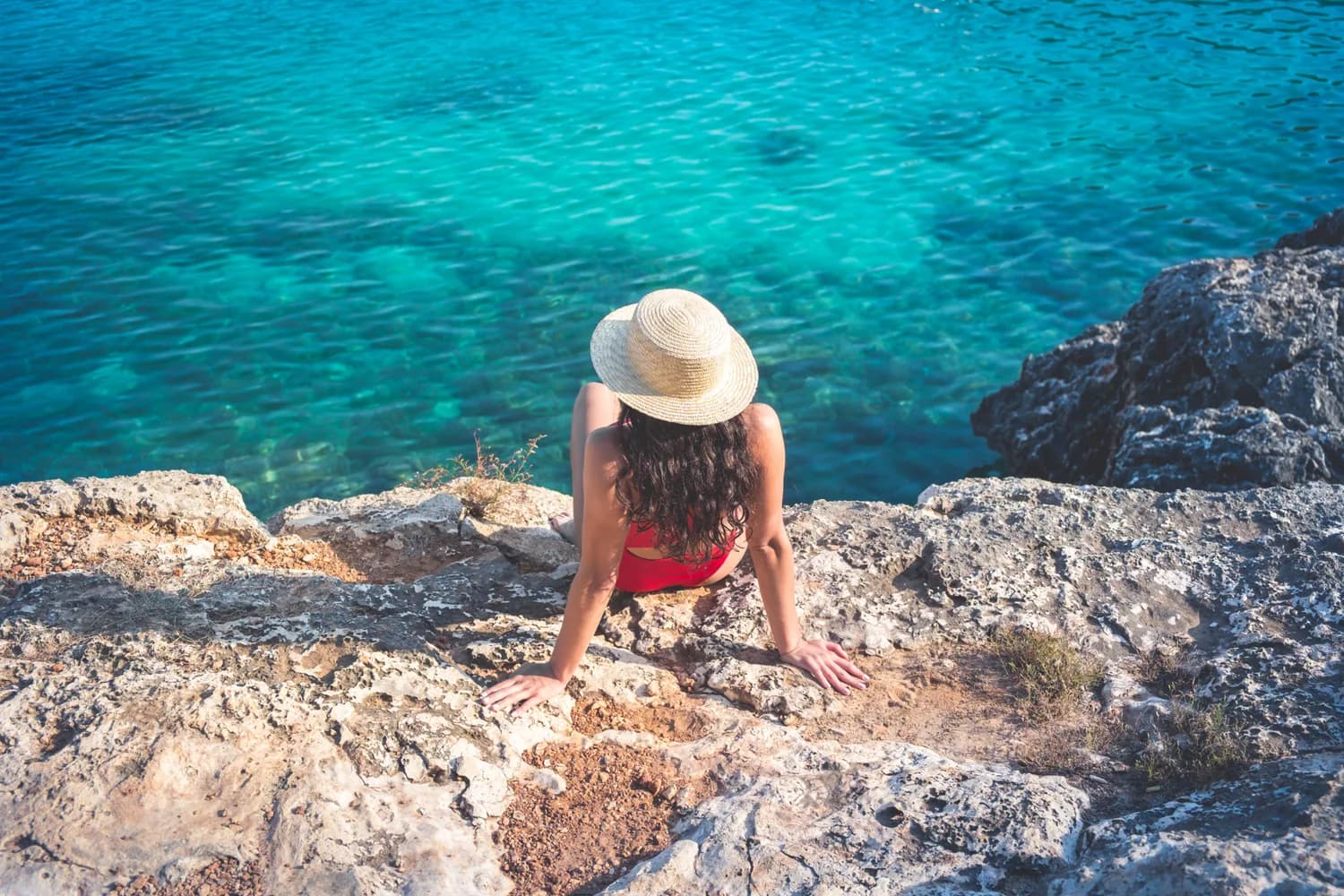 Frau in rotem Bikini und Sonnenhut an einem Strand auf Mallorca