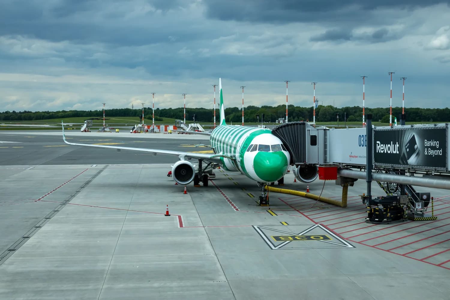 Passagierflugzeug in grüner Lackierung am Abflug-Gate am Flughafen Hamburg, Fluggastbrücke angedockt und Bodenfahrzeuge bereit