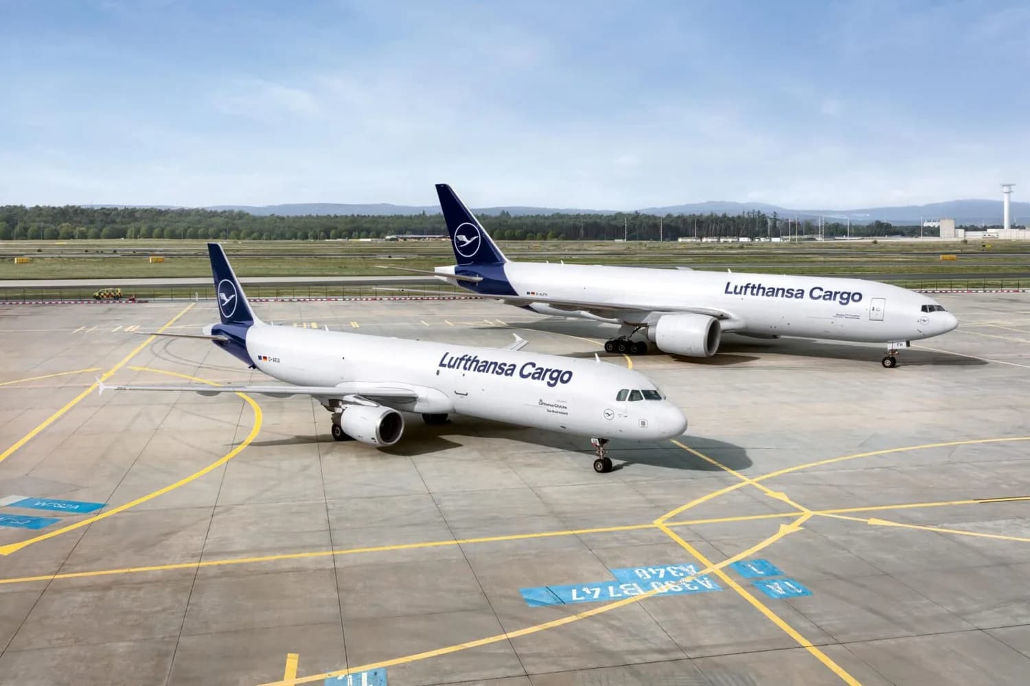 Zwei Lufthansa Cargo Frachtflugzeuge (A321F im Vordergrund, B777F im Hintergrund) auf dem Rollfeld eines Flughafens, geparkt und bereit zum Beladen.