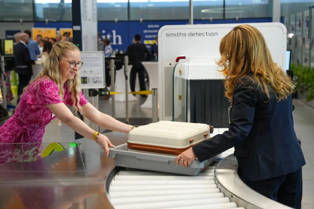 Frau legt Koffer in Plastikwanne am Sicherheitskontrollscanner am Flughafen, Mitarbeiterin überwacht Röntgenanlage und Gepäckdurchleuchtung