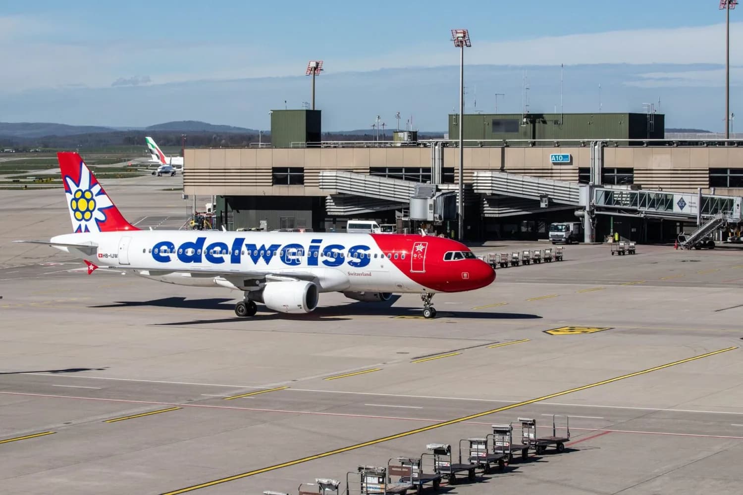 Edelweiss Air Passagierflugzeug am Gate am Flughafen Zürich, rot-weißes Flugzeug mit Edelweiß-Logo auf dem Heck und Passagierbrücken im Hintergrund