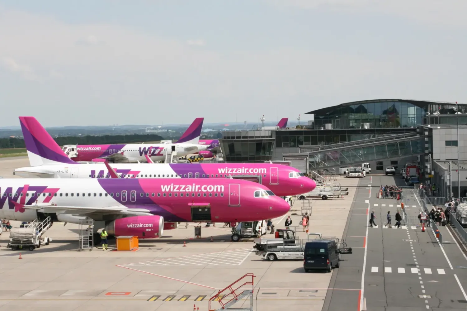 Flughafen-Gate mit mehreren pink-violetten Wizz Air Flugzeugen am Terminal, Boarding und Bodenbetrieb mit Passagieren und Rampenfahrzeugen
