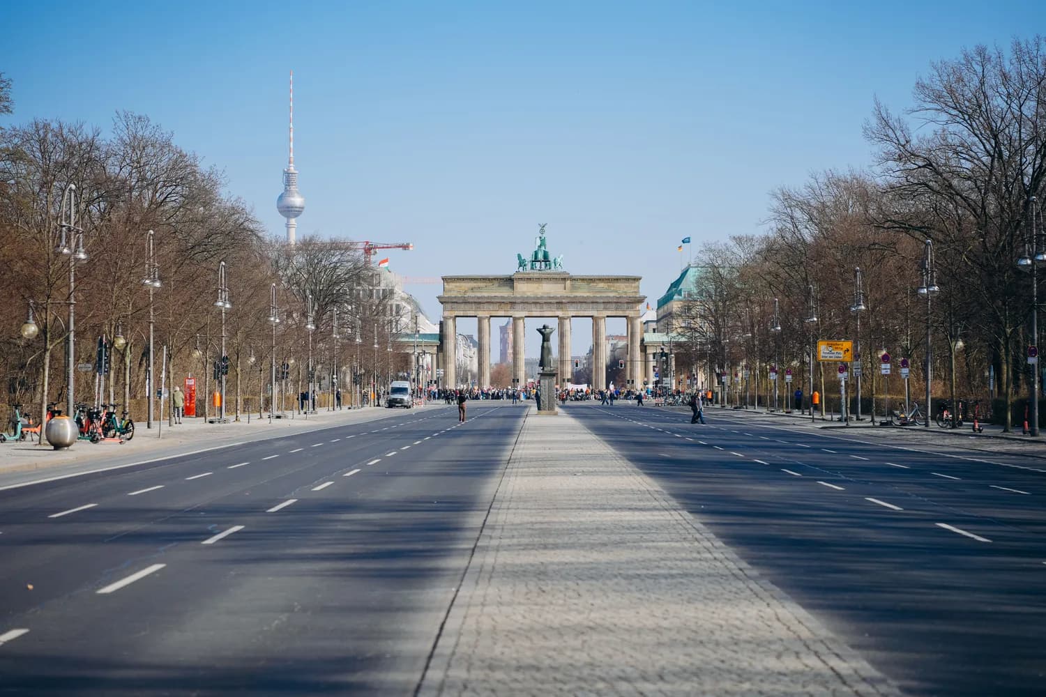Brandenburger Tor im Berliner Straßenpanorama mit Fernsehturm im Hintergrund und menschenleerer Fahrbahn