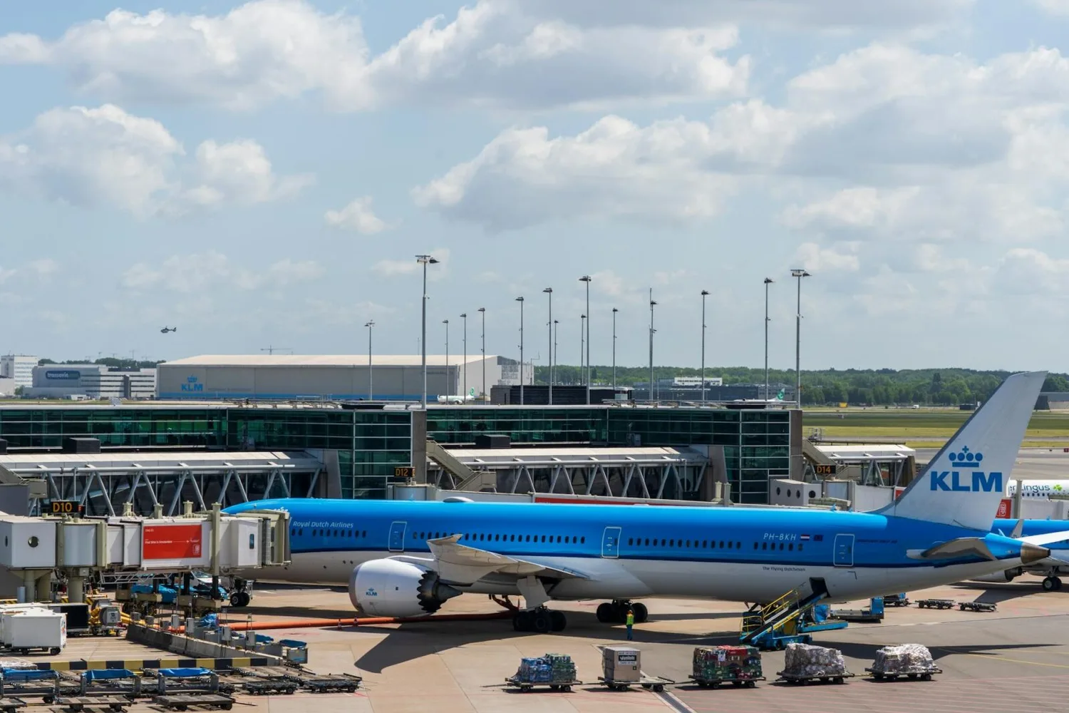 KLM Passagierflugzeug an Gate am Flughafen Schiphol mit Fluggastbrücke, Bodenpersonal und Gepäckwagen vor Terminalgebäude