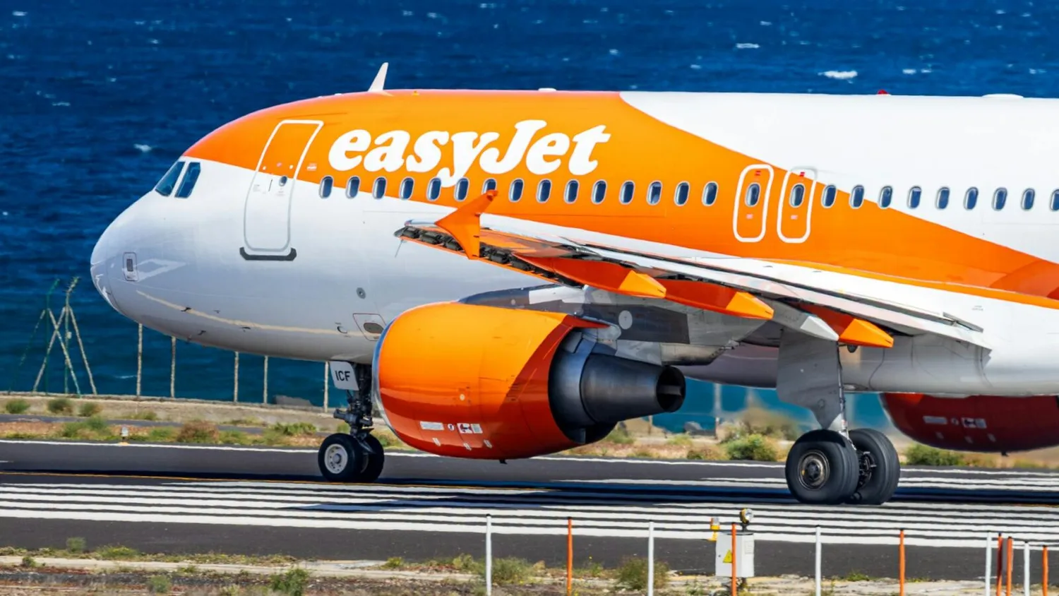 easyJet Passagierflugzeug in orange-weißer Lackierung beim Rollen auf der Startbahn am Meer