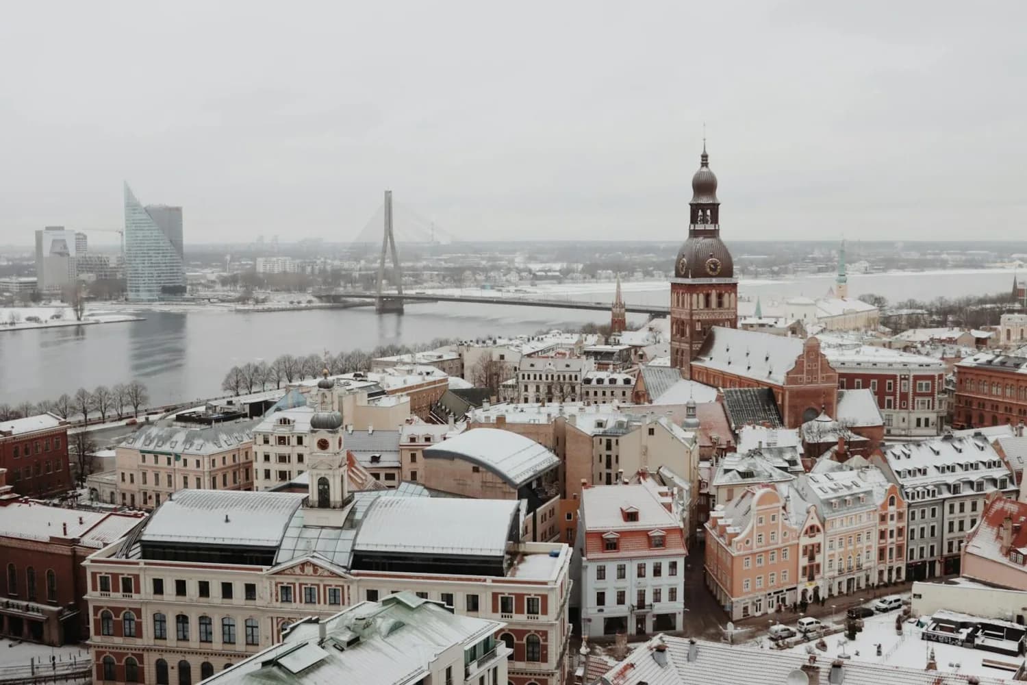 Vogelperspektive auf verschneite Altstadt von Riga mit Domturm, Daugava-Fluss und modernen Geschäftsgebäuden im Hintergrund