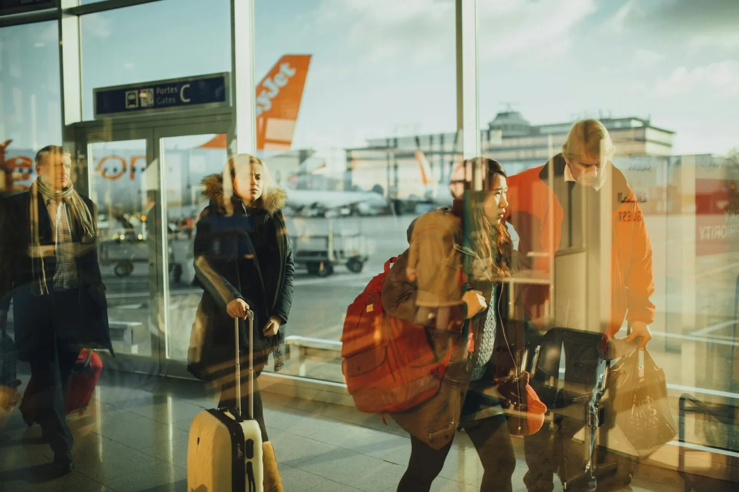 easyJet-Passagiere mit Handgepäck und Rollkoffer am Flughafenterminal vor Flugzeug im Hintergrund