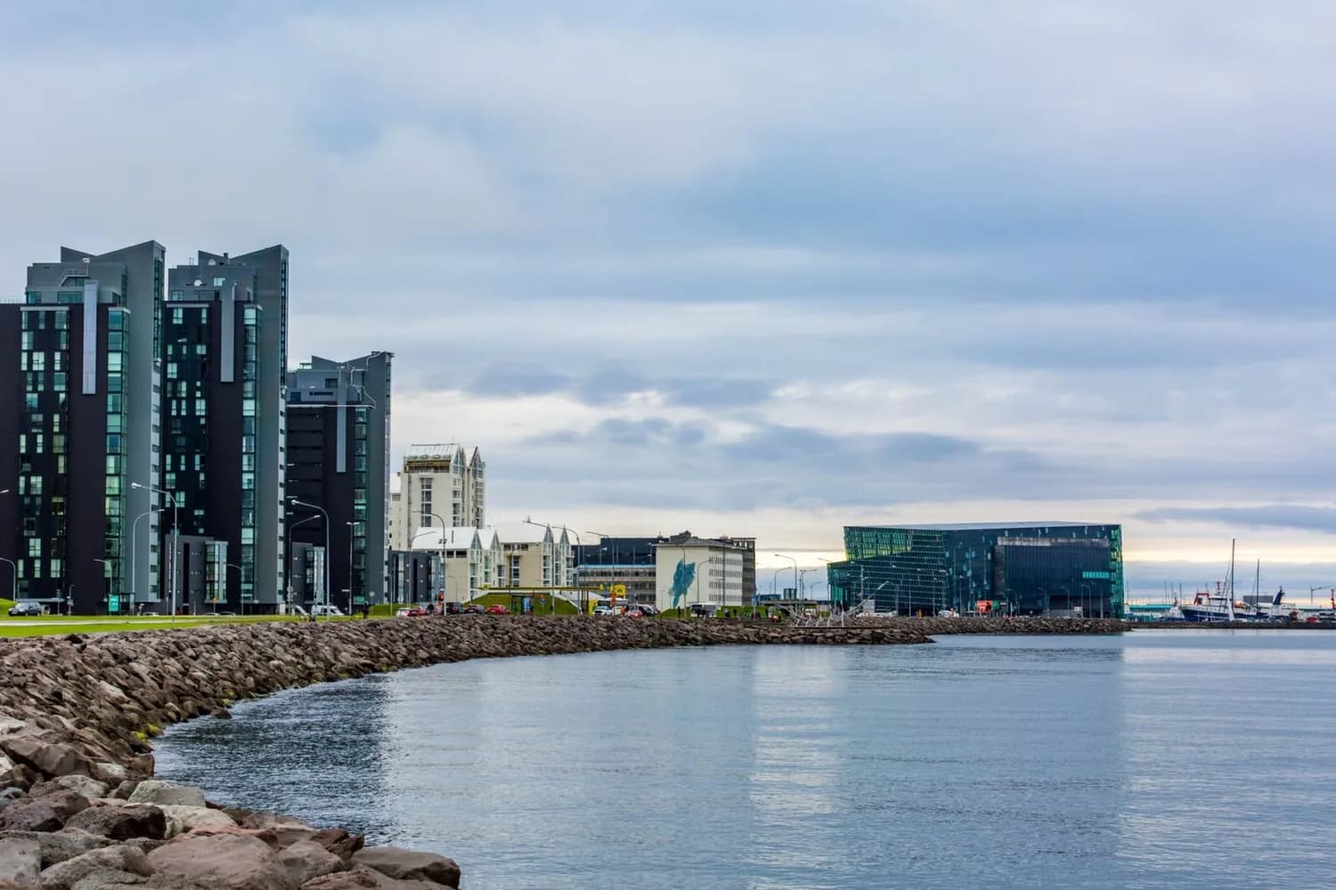 Reykjavik Hafenpromenade mit modernen Wohnhochhäusern, Harpa Konzerthalle aus Glas und ruhiger Buchtfront bei bewölktem Himmel