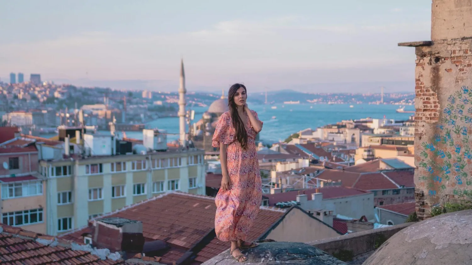 Frau im sommerlichen Maxikleid auf einem Dach mit Blick auf Istanbuls Bosporus, Moschee und Stadtpanorama
