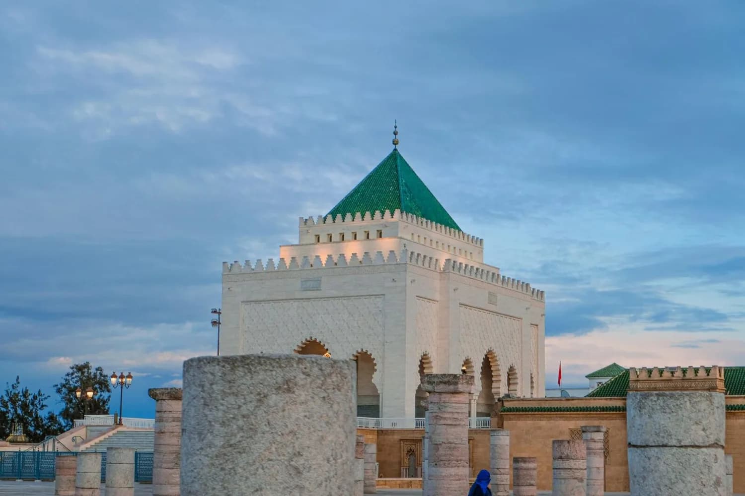Mausoleum von Mohammed V in Rabat, Marokko mit weißem Sandsteinbau, grünem Pyramidendach und Säulenresten im Vordergrund