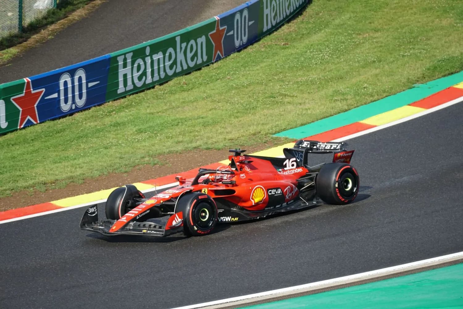 Rotes Ferrari Formel‑1‑Rennauto mit Fahrer auf Rennstrecke, Werbebanden und grün‑gelb‑roten Curbs sichtbar