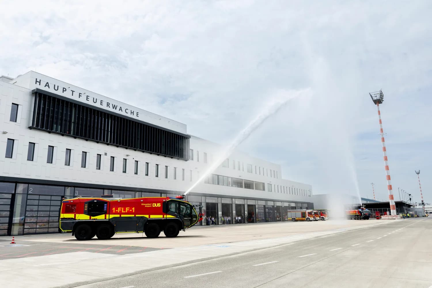 Hauptfeuerwache Flughafen Düsseldorf mit neuem Löschfahrzeug vor Toren und Wasserfontänen zur Einweihung